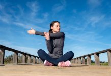 Schultergürtel verspannt trotz Bewegung Frau sitzt nach dem Sport auf einer Holzbrücke im Freien und dehnt sich an der Schulter
